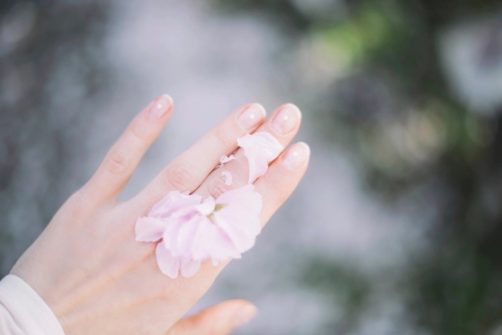 Mano con las uñas pintadas y pétalos de flor